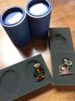 Two Swarovski crystal ornaments in blue cylindrical boxes with foam inserts, one elf and one moose on skis.