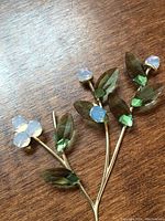 Close-up photo of the Swarovski mistletoe figurine showing translucent green crystal leaves and opaque white crystal berries on gold-tone stems against a wooden background.