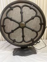 Front view of the Flatiron Model E3 Bluetooth speaker showing textured black metal grill and beige fabric cover with central badge.