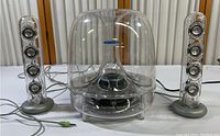 Front view of the whole Harman Kardon SoundSticks II speaker system including the transparent subwoofer and two satellite speakers with visible wiring and 3.5 mm audio jack.