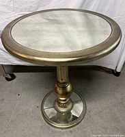 Front angled view showing the weathered mirrored glass top with a golden-bronze metal frame and pedestal base.