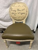 Front view of Pearson chair showing padded olive green vinyl seat and fabric back cushion with vintage script print, and white distressed wooden frame.