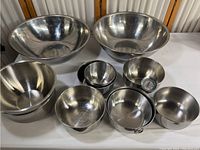 Wide shot of 8 stainless steel bowls displayed on table showing size range and reflective finish