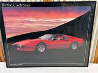 Framed vintage Ferrari 308 poster on display showing car against sunset sky with 'The Rod Caudle Series' text at top left.