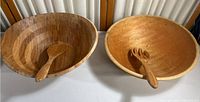 Wood salad bowls with serving utensils shown side by side on a surface.