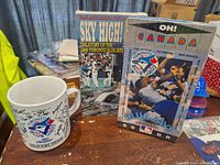 Photo shows two Toronto Blue Jays VHS tapes and one vintage ceramic mug with Blue Jays logo and signatures on the table.