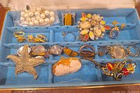 Blue velvet-lined jewelry box holding various costume jewelry pieces distributed in compartments