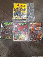 Four comic books laid out on wooden floor, three Spawn comics and one A-Team comic