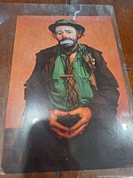 Front of the vintage clown postcard showing a sad clown in a hat and colorful clothes with hands held together.