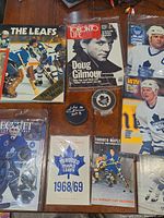 Collection of assorted Toronto Maple Leafs memorabilia items including signed pucks, vintage magazine covers, photographs, and pamphlet.