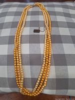 Full view of the double strand faux pearl necklace laid out on a checkered grey and white surface showing the alternating golden and light pearl strands.