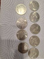 Top view of 8 Olympic coins arranged vertically on white paper towel, showing sport-themed designs and wear.
