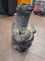 Front and side view of the polar bear sculpture holding a child, showing detailed carving and weathered surface.