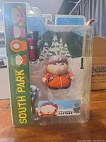 Front view photo of South Park Eric Cartman figure in original blister pack with cardboard backing. Figure is dressed in orange winter jacket. Packaging has South Park character icons visible.