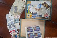 Photo showing two open boxes with assorted vintage postage stamps in various conditions and designs including Canadian stamps.
