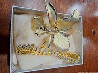 Top-down photo of vintage gold-tone butterfly brooch and rhinestone bracelet in small display box.