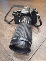 Front angle view of Ricoh KR-5 camera with long Ricoh Pentax-A 200mm lens and strap on floor surface.