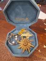 Opened blue-grey Birks suede octagonal jewelry box showing three vintage brooches