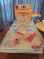 Front view of vintage electric pinball table top game showing clear plastic top with metal bumpers and red flippers.