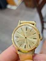 Close-up of vintage Timex wristwatch showing gold tone case, dial, and expandable metal band.