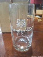 Closeup of one whiskey glass showing Canadian Club crest and text "Canadian Club C.C." in white on clear glass.