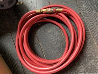 Coiled 25ft red air hose with brass quick connect fittings on wooden floor.