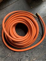 Coiled orange 50 ft air hose shown on wooden surface.