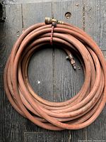 Top-down photo of coiled long orange/red air hose with brass connector ends on a wooden surface.