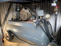 Full side view of the air compressor showing gray horizontal tank, wheels, motor, and power cord.