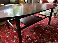 Solid cherry wood coffee table with smooth polished surface and lower shelf on a red patterned rug.