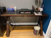 Wood desk shown with various office items on and around it including a Toshiba laptop, mouse on a mousepad, cups with pens and pencils, a book, and a wastebasket. The top has a tinted black glass surface inset into the wood frame.