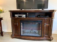 Full view of the cherry finish solid wood fireplace TV stand with TV on top, storage compartments, and electric fireplace insert in the center.