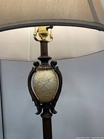 Close-up of upper part of the floor lamp showing the ornate decorative glass center with a cracked or textured pattern, surrounded by dark wood or metal components and topped by the lamp fitting and shade.