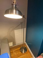 Silver floor lamp illuminated, showing the dome-shaped shade and articulating arm.