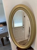 Full view of the large gold oval mirror standing against a wall, showing beveled edged glass and gold frame with inner beaded detailing.