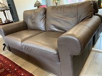 Front and side view of brown leather loveseat showing rolled arms and cushions