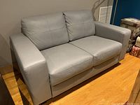 Front view of grey leather loveseat on hardwood floor