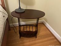 Front angle view of the solid wood oval magazine table with magazine rack below the tabletop.
