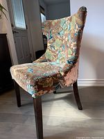 Side view of a single pier one velvet upholstered chair showing fabric pattern, embroidered back and wooden legs.