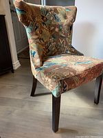 Front and side view of a wingback style velvet upholstered accent chair with multicolor floral pattern on seat and wings, dark wood legs visible.