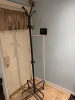 Full view of black rod iron coat rack standing next to an entrance door showing its hooks and overall height.