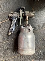 Overall photo of the Binks spray paint gun showing metal paint container and black handle with trigger and nozzle assembly.