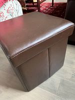 Foot stool showing brown, smooth textured top with some wear and stitching along edges.