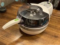 White compact T-Fal Actifry air fryer with folding handle extended on a wooden table, showcasing transparent lid and control panel on top.