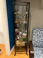 Front view of the tall glass door iron display cabinet filled with various decorative items showing the overall structure and condition.