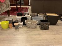 Photo showing the full set of 18 assorted clay pots and planters arranged in rows on a wooden floor.