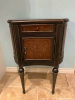 Front view of dark wood cabinet showing top drawer and lower door with decorative carved floral pattern.