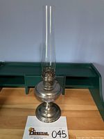 Full view of the Aladdin No. 11 oil lamp with tall glass chimney and polished metal base.