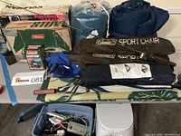 Full lot showing camping chairs, sleeping bags, stove boxes, and portable toilet on a table