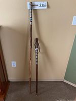 Two German wooden walking sticks side by side showing full length against a wall, highlighting height difference and overall appearance.